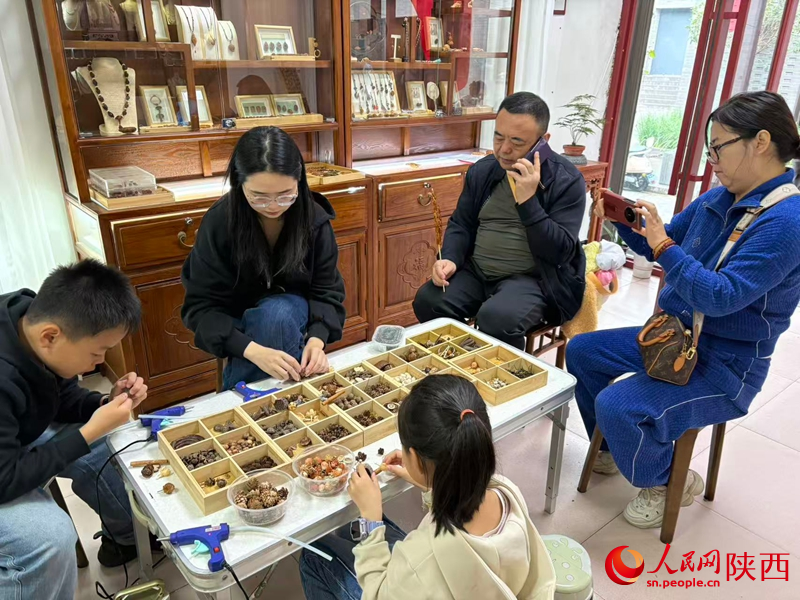 游客正在挑選果核，體驗(yàn)核雕技藝。人民網(wǎng) 王麗攝